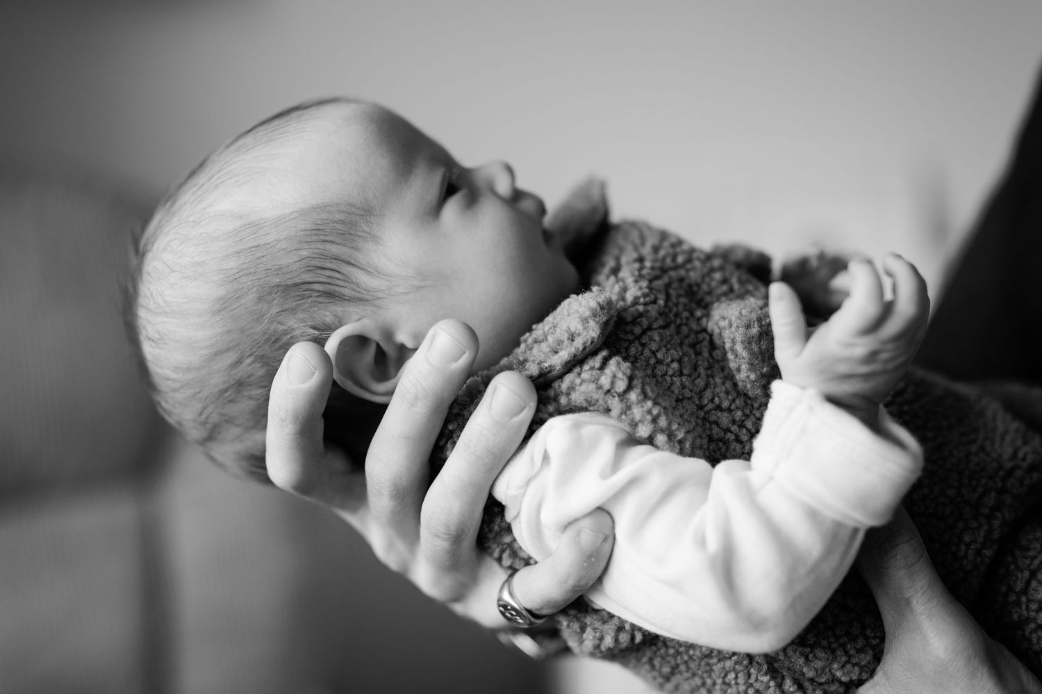 Black and white photo of a sleeping newborn baby cradled in an adult's hand, wearing a soft knit sweater and white sleeves.