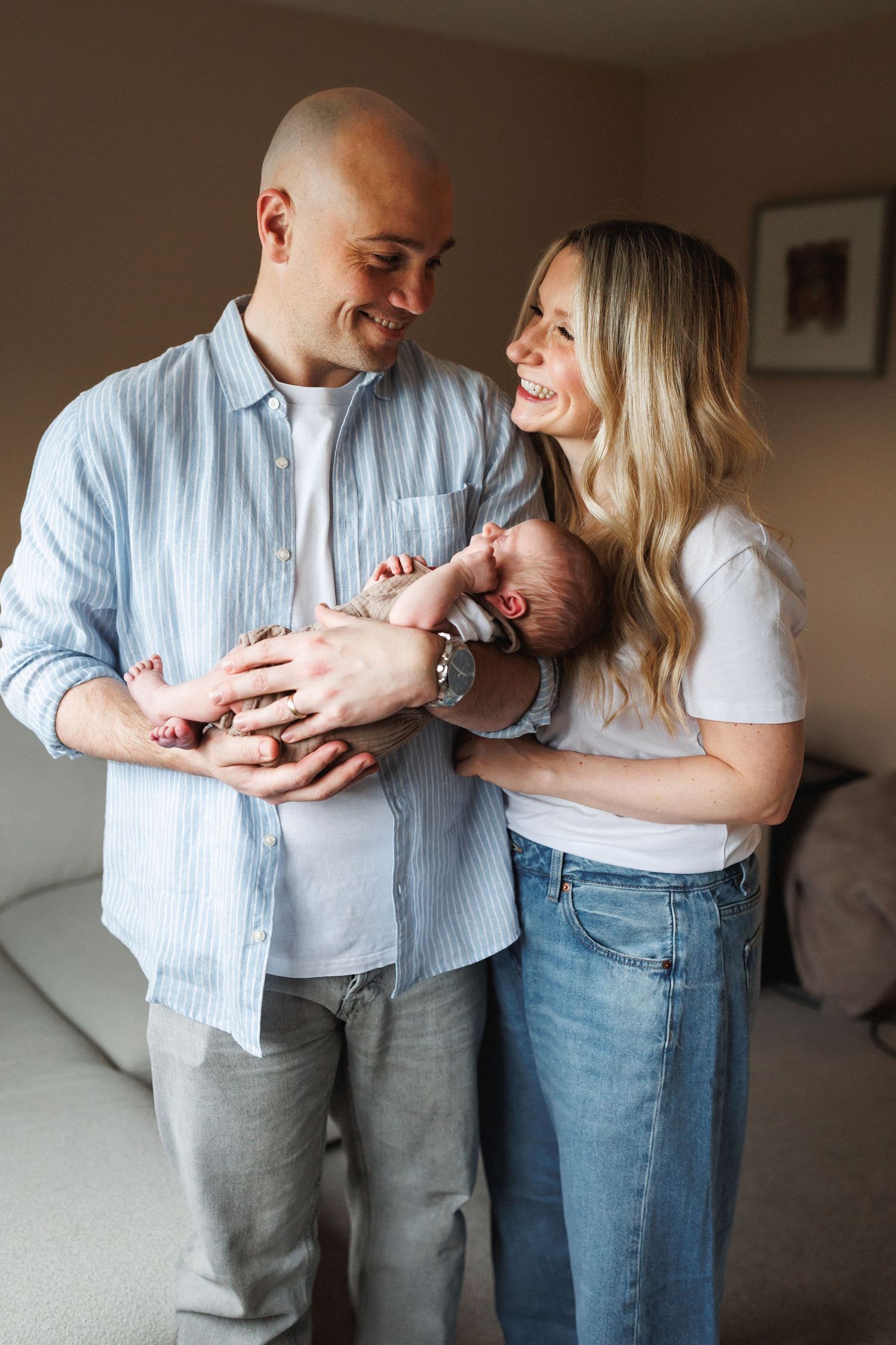 Happy couple smiling at each other while gently holding their newborn baby at home.