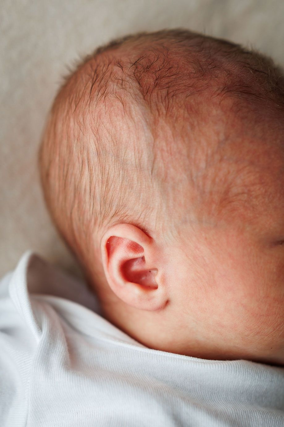 Close-up side profile of a newborn baby's head showing delicate ear and fine hair.