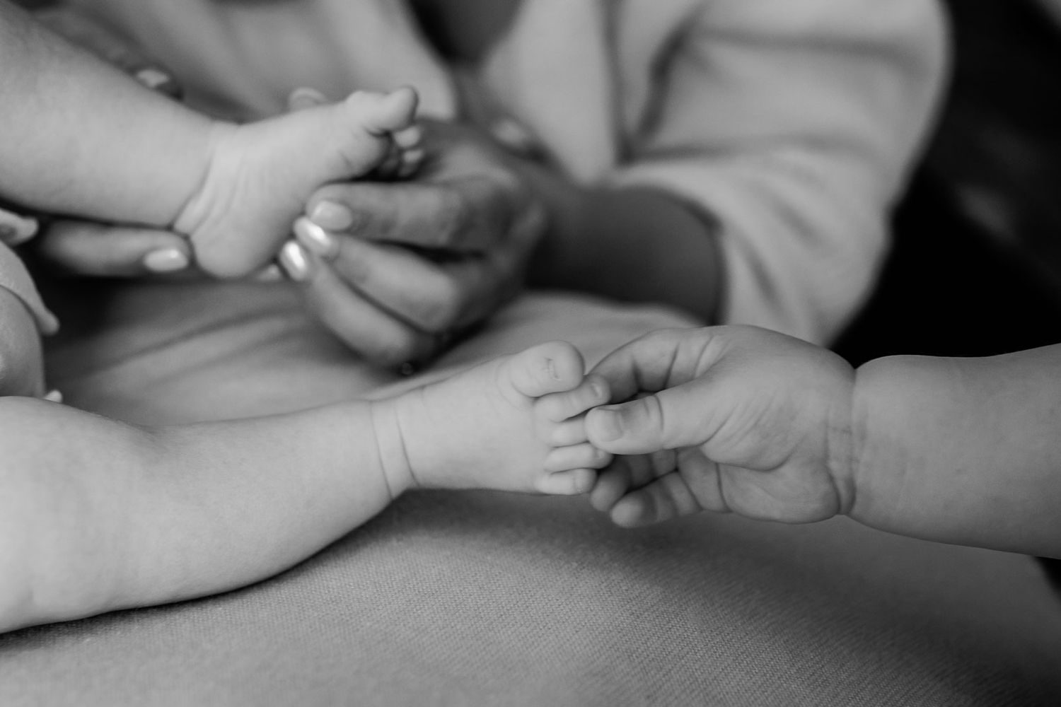 Black and white close-up of newborn baby hands and feet gently held by parents.