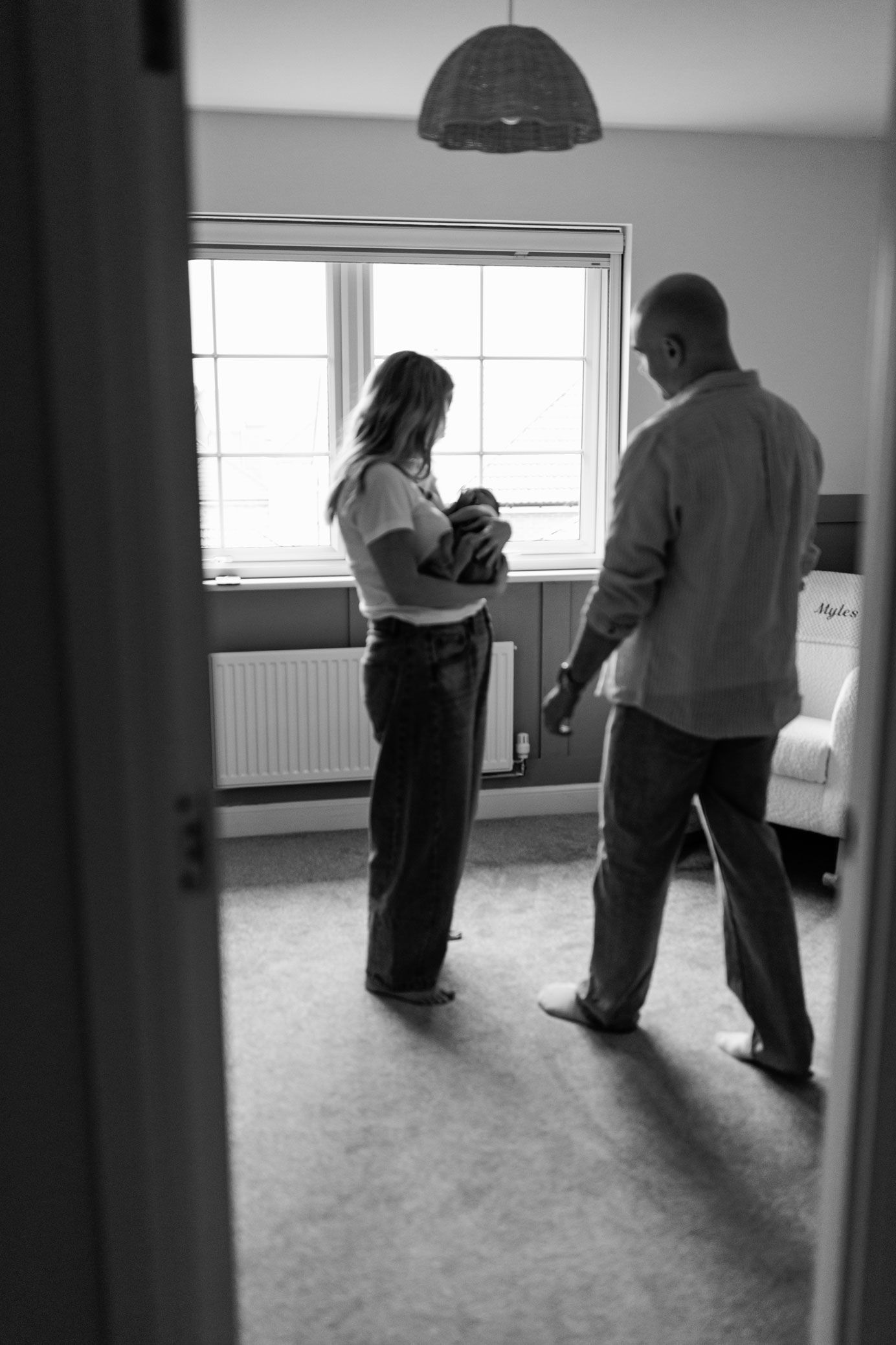 Black and white photo of parents admiring their newborn baby by a window in their Nottingham Newborn Session