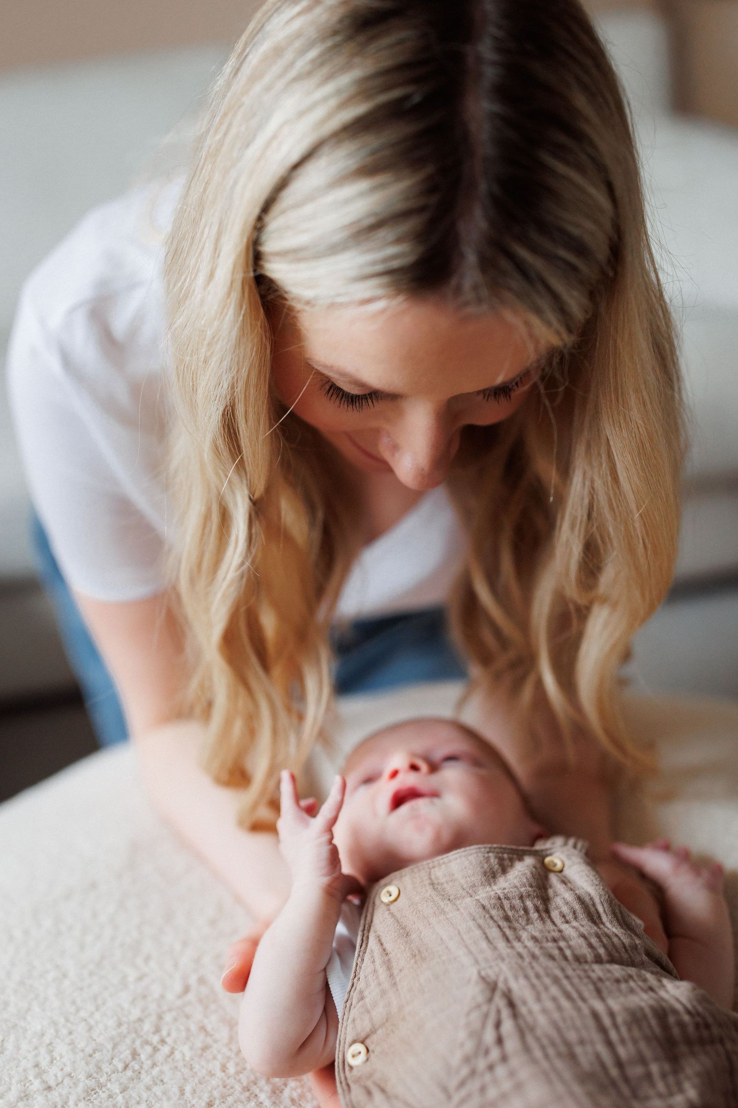 Blonde mother leaning over to gaze lovingly at her newborn baby lying on a blanket.