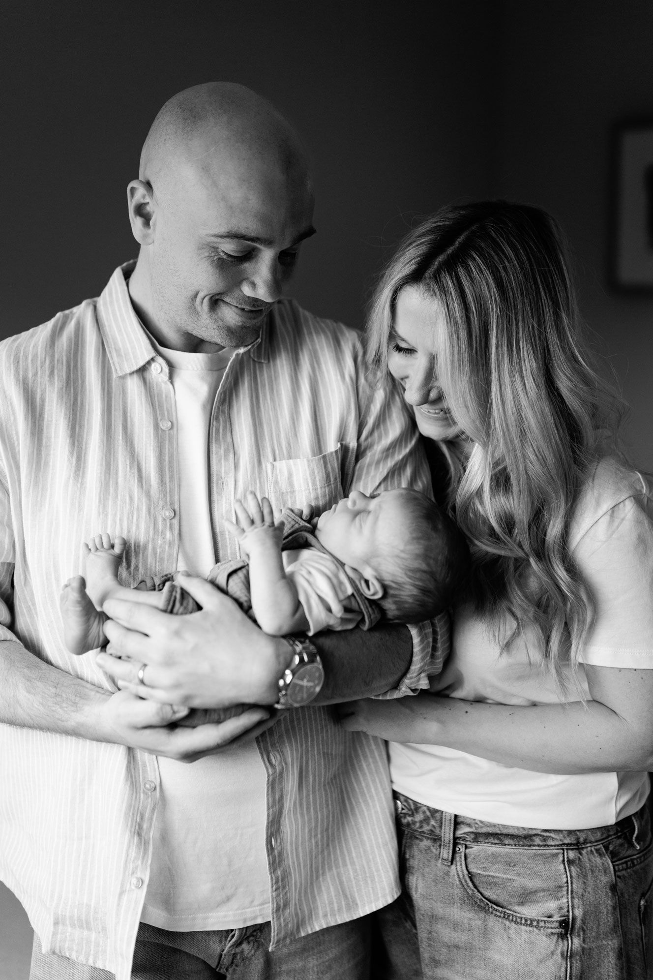Black and white photo of smiling parents lovingly holding their newborn baby together indoors in their Nottingham Newborn Photo Session