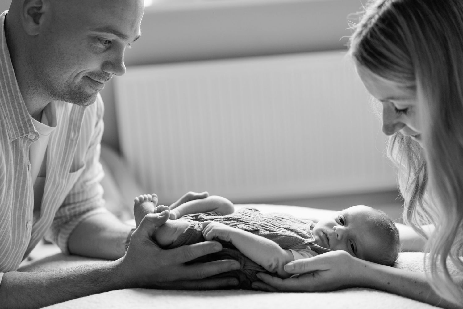 Black and white photo of parents lovingly gazing at their newborn baby lying between them in their Nottingham Newborn Session