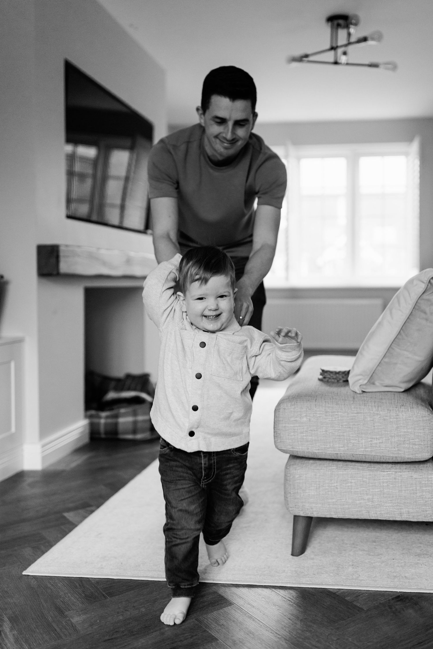Black and white photo of father playing with laughing toddler son in living room.