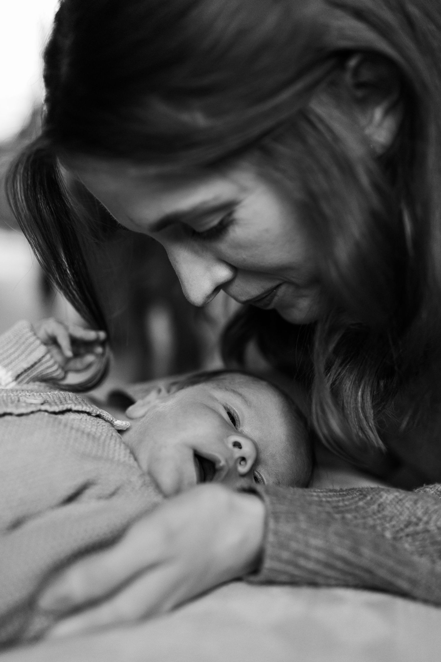 Black and white close-up of a mother tenderly gazing at her sleeping newborn baby held in her arms.