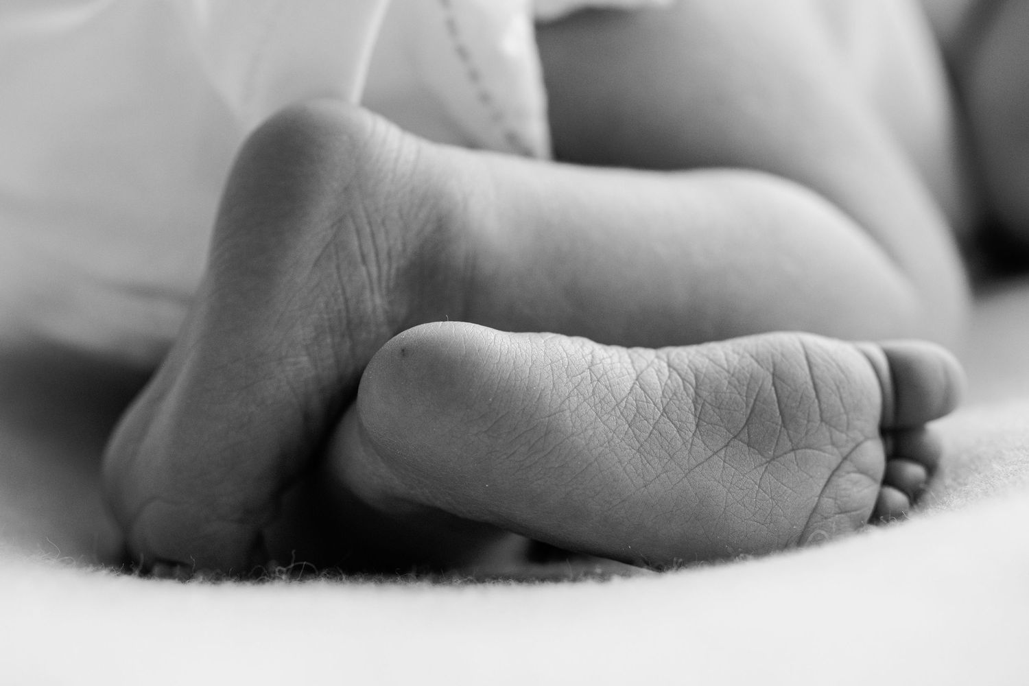 Detailed black and white close-up of tiny newborn baby feet resting on soft white surface.