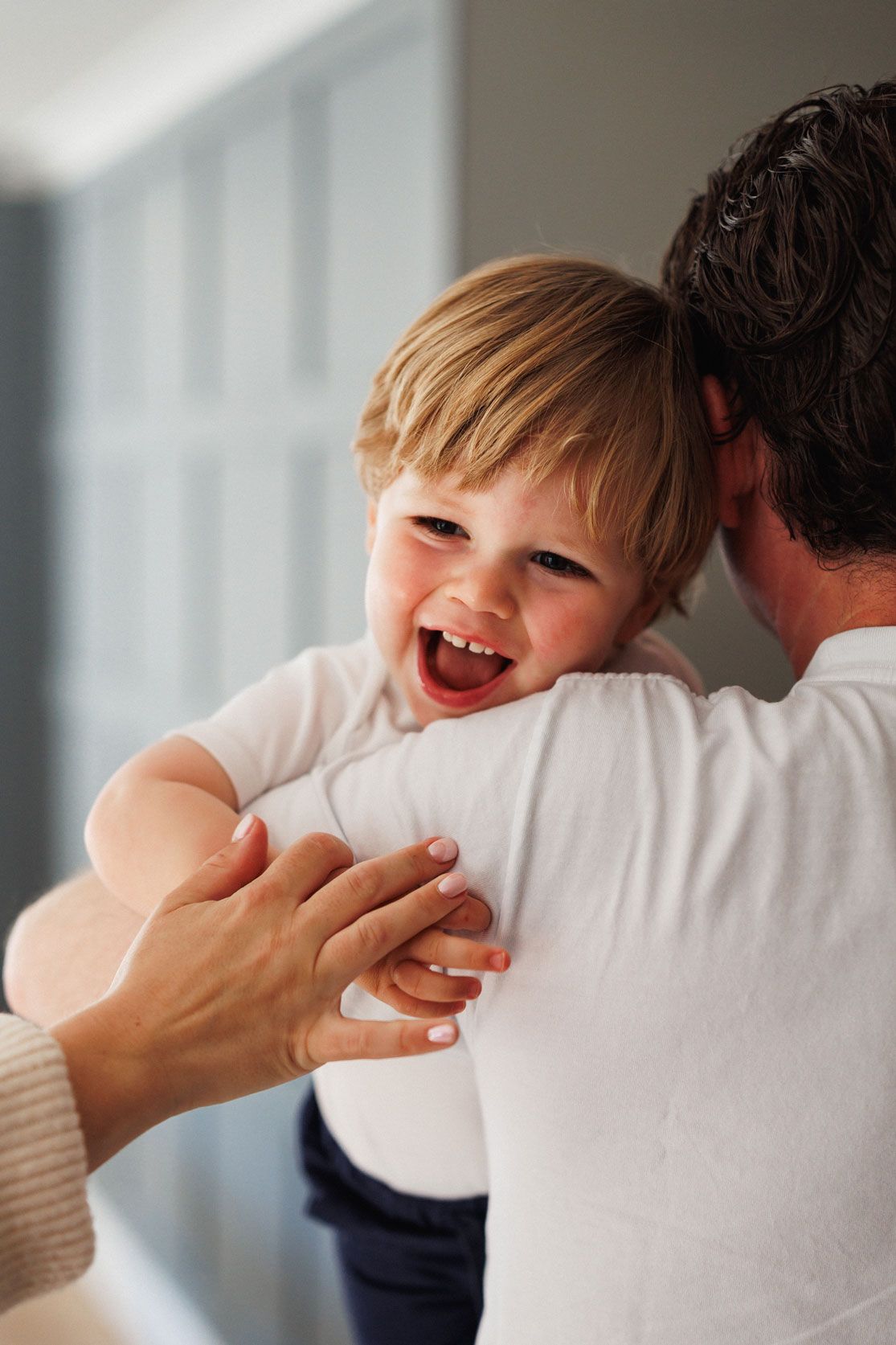 Happy toddler laughing joyfully while being held by a parent indoors.