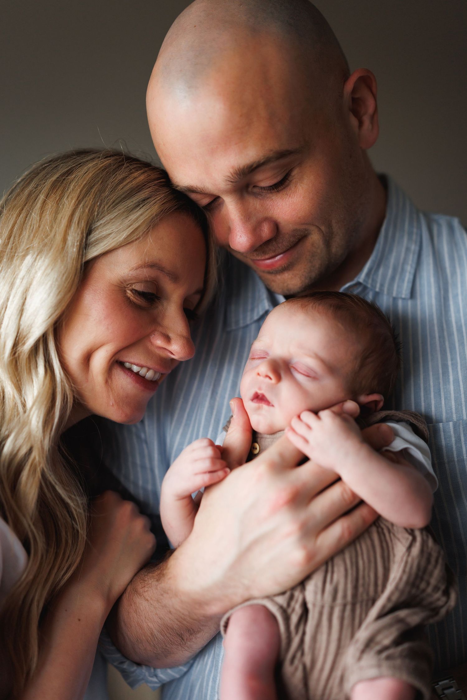 Loving parents smiling and holding their sleeping newborn baby close in a warm portrait.