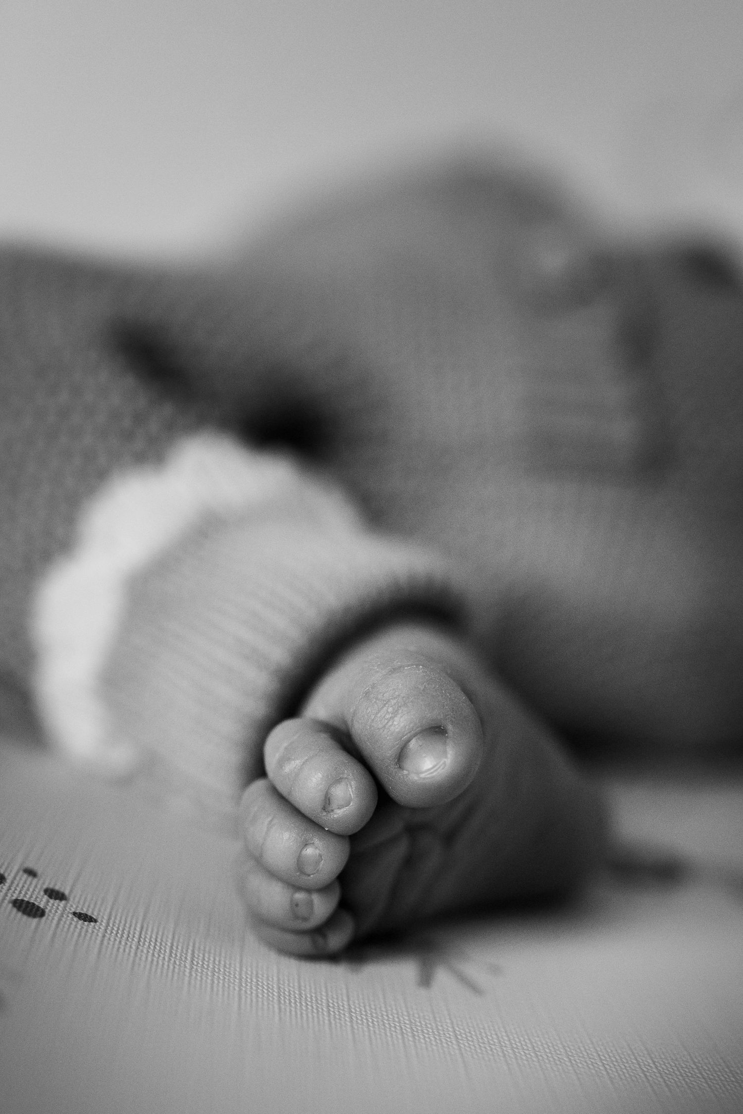Black and white macro photo of a sleeping newborn baby's tiny feet in a knit onesie.
