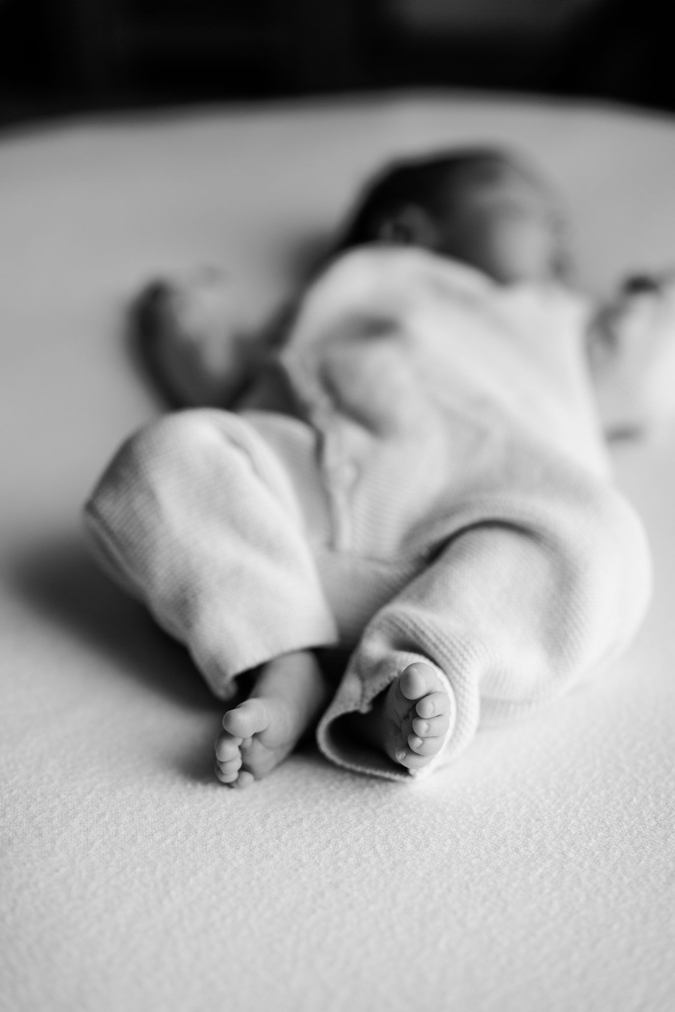 Black and white photo of a sleeping newborn baby in soft knit clothing, with tiny bare feet in sharp focus on a cozy blanket.