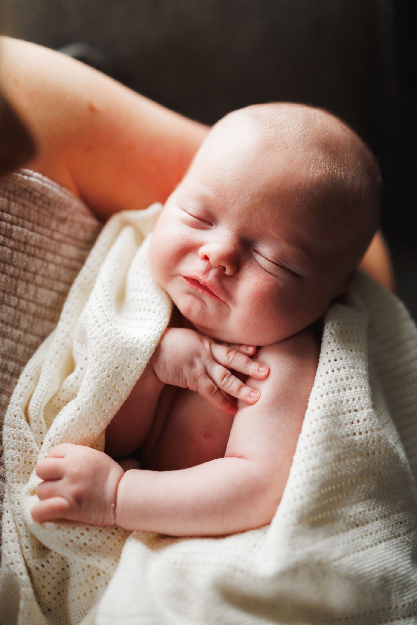 Peaceful newborn baby sleeping wrapped in a soft white knit blanket, cradled in an adult's arms.