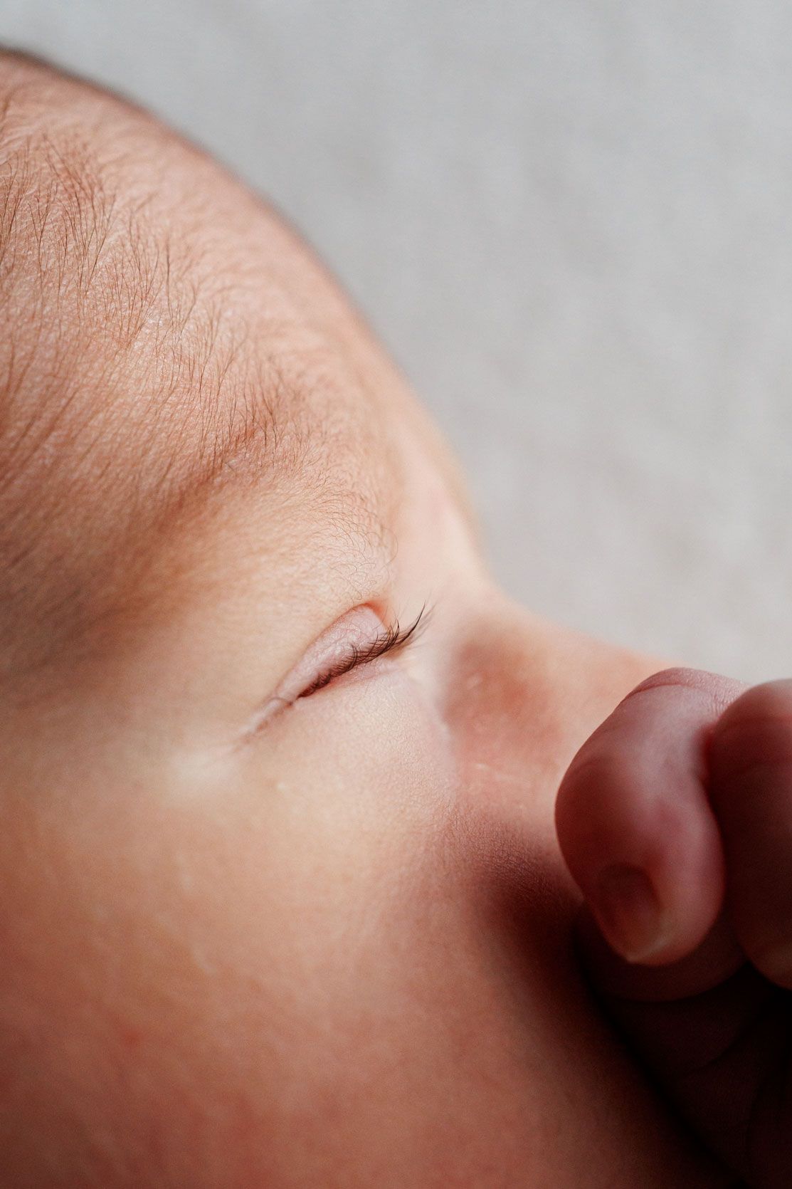 Close-up side profile of a sleeping newborn baby with closed eyes and long lashes, a tiny fist resting near the nose.