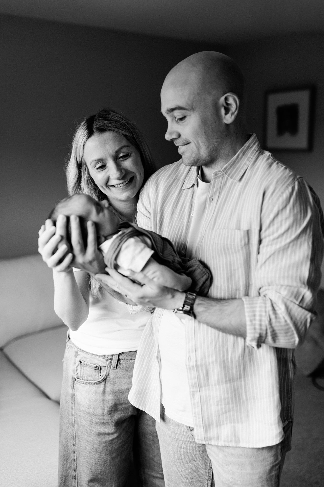 Black and white photo of smiling parents holding their newborn baby together in a cozy bedroom in their Nottingham Newborn Session