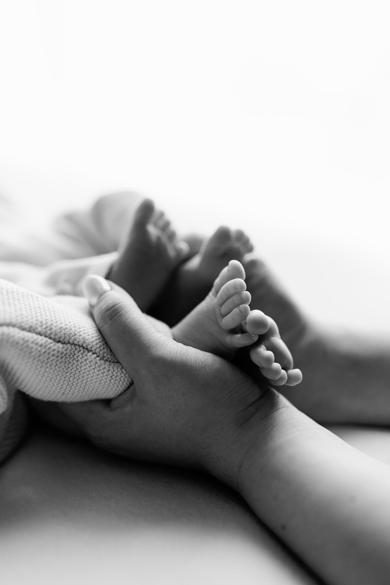 Black and white photo of a parent's hand gently holding a newborn baby's tiny feet on a soft blanket.