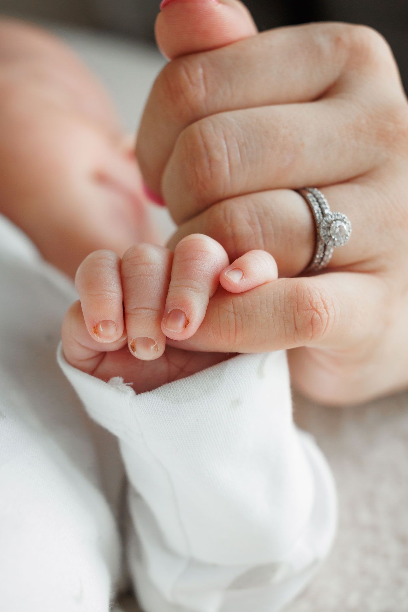 Close-up of a newborn baby's tiny hand gripping a mother's finger with a diamond ring.