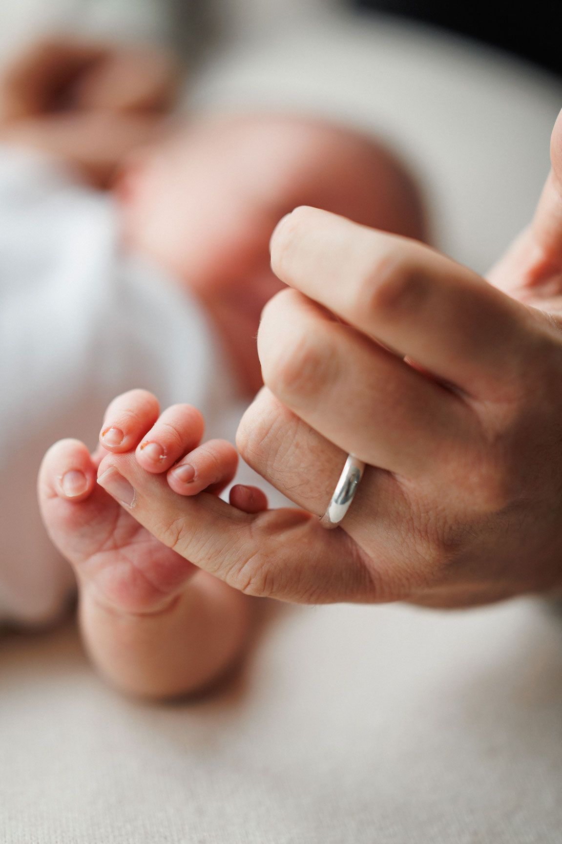 Close-up of a parent's ringed hand gently holding a newborn baby's tiny feet.