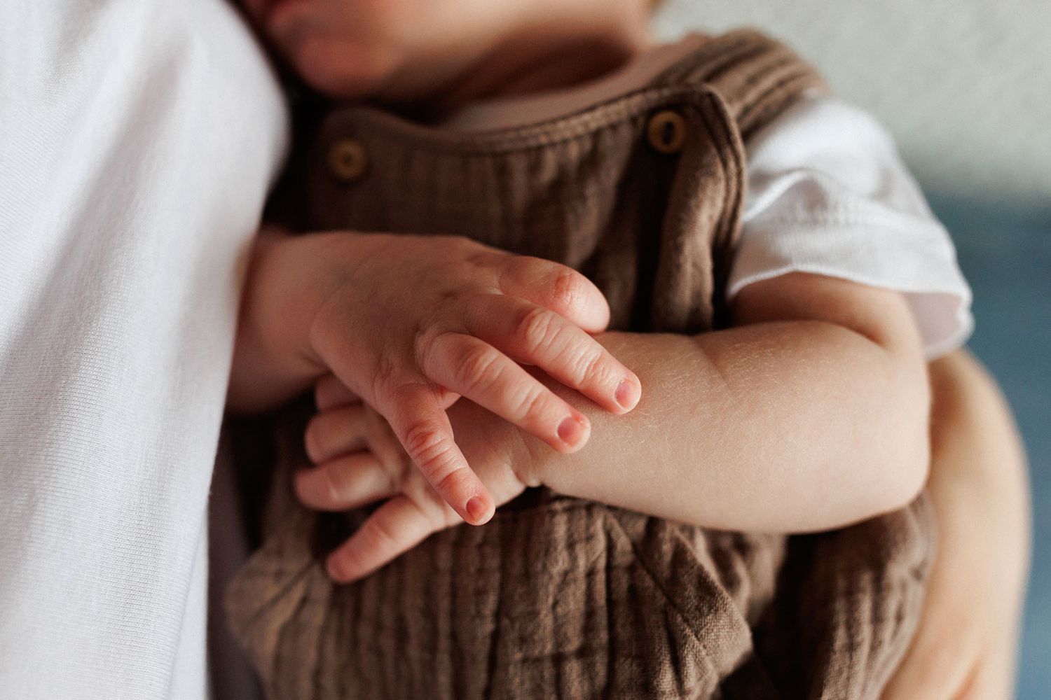 Close-up of a baby's tiny hands resting on brown linen overalls, capturing delicate newborn fingers in soft natural light in Nottingham