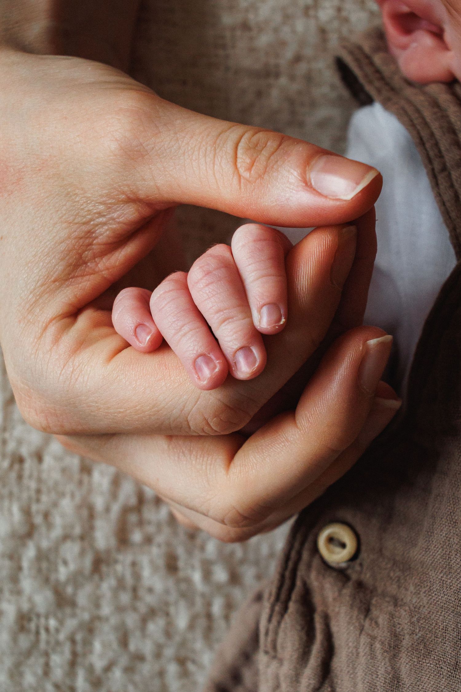 A newborns tiny hand gently grips an adults finger in a tender close-up photo.