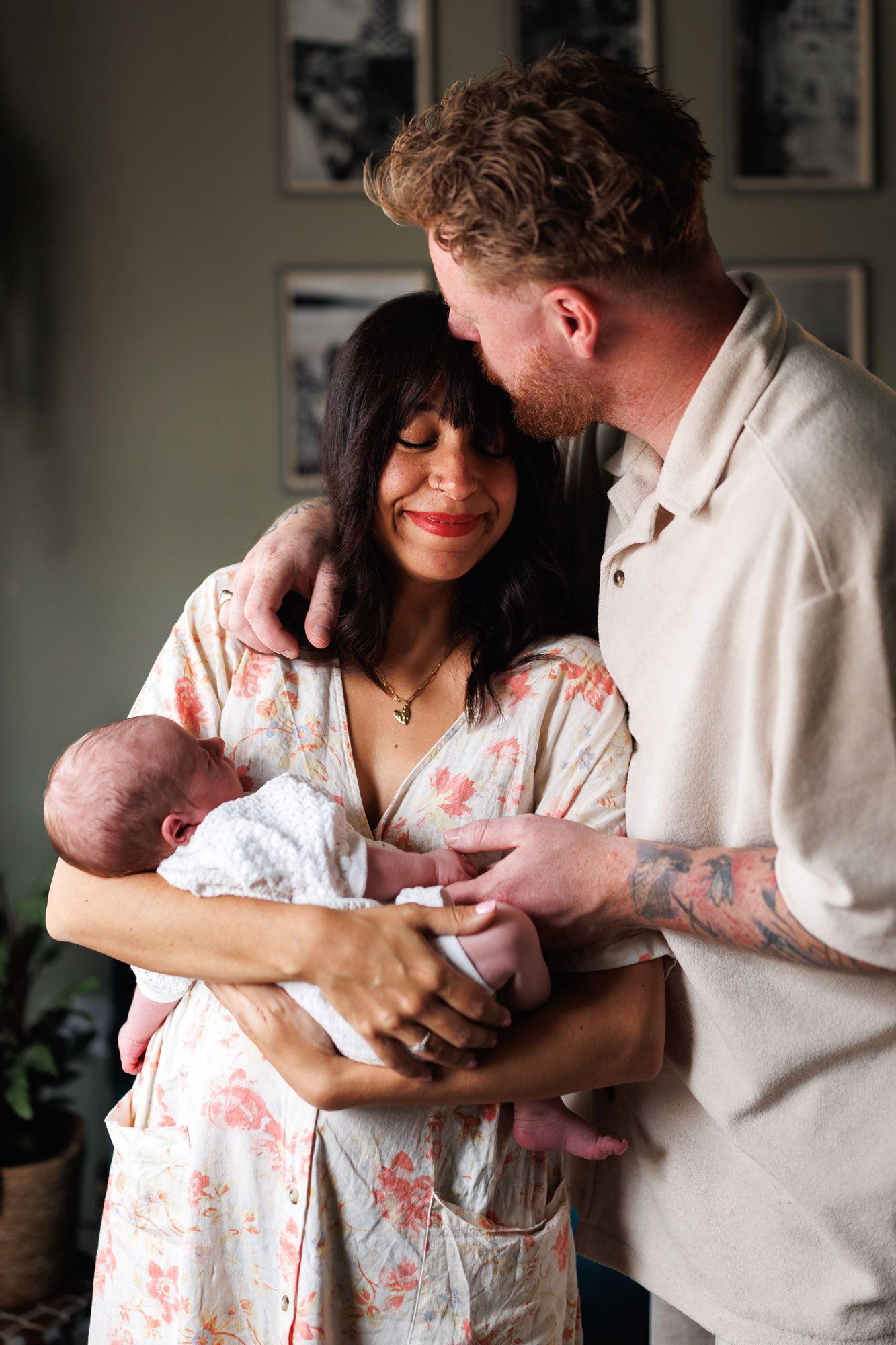 Happy couple smiling and embracing while holding their newborn baby at home.