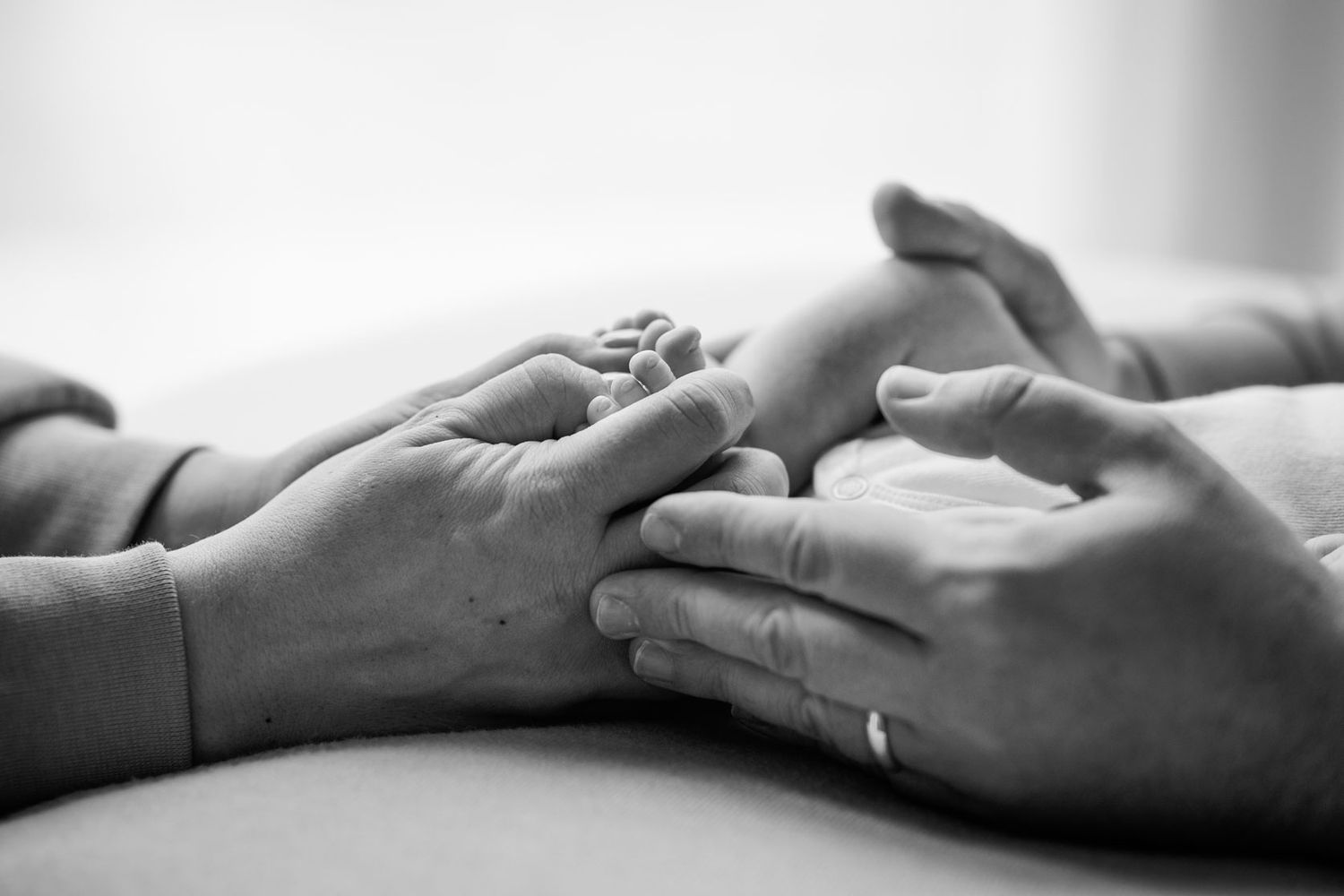 Black and white photo of adult hands gently cradling a newborn baby's tiny feet together.