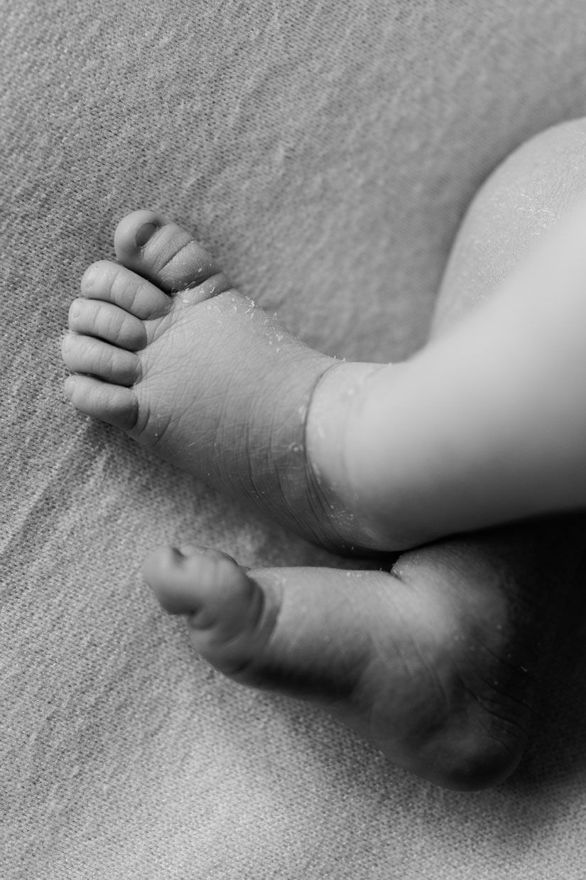 Black and white close-up of tiny newborn baby feet crossed on a soft textured blanket.