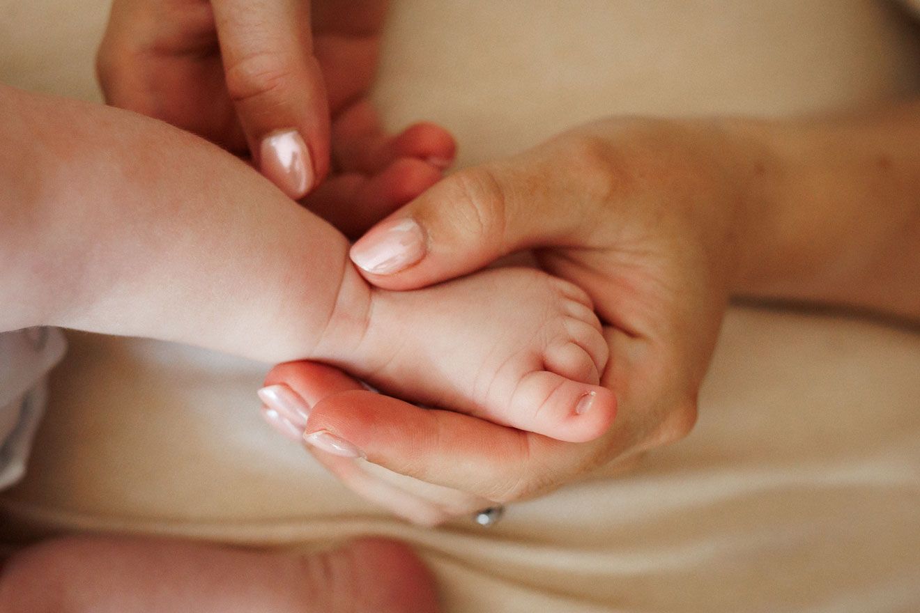 Close-up of a mother's manicured hands tenderly holding her newborn baby's tiny feet.