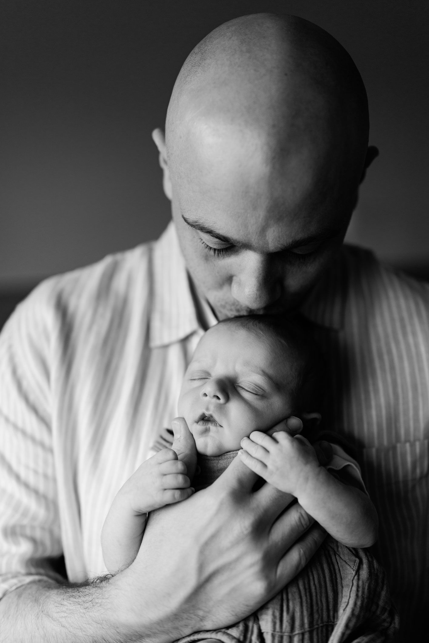 Black and white photo of a bald father kissing his sleeping newborn baby in their Nottingham Newborn Session