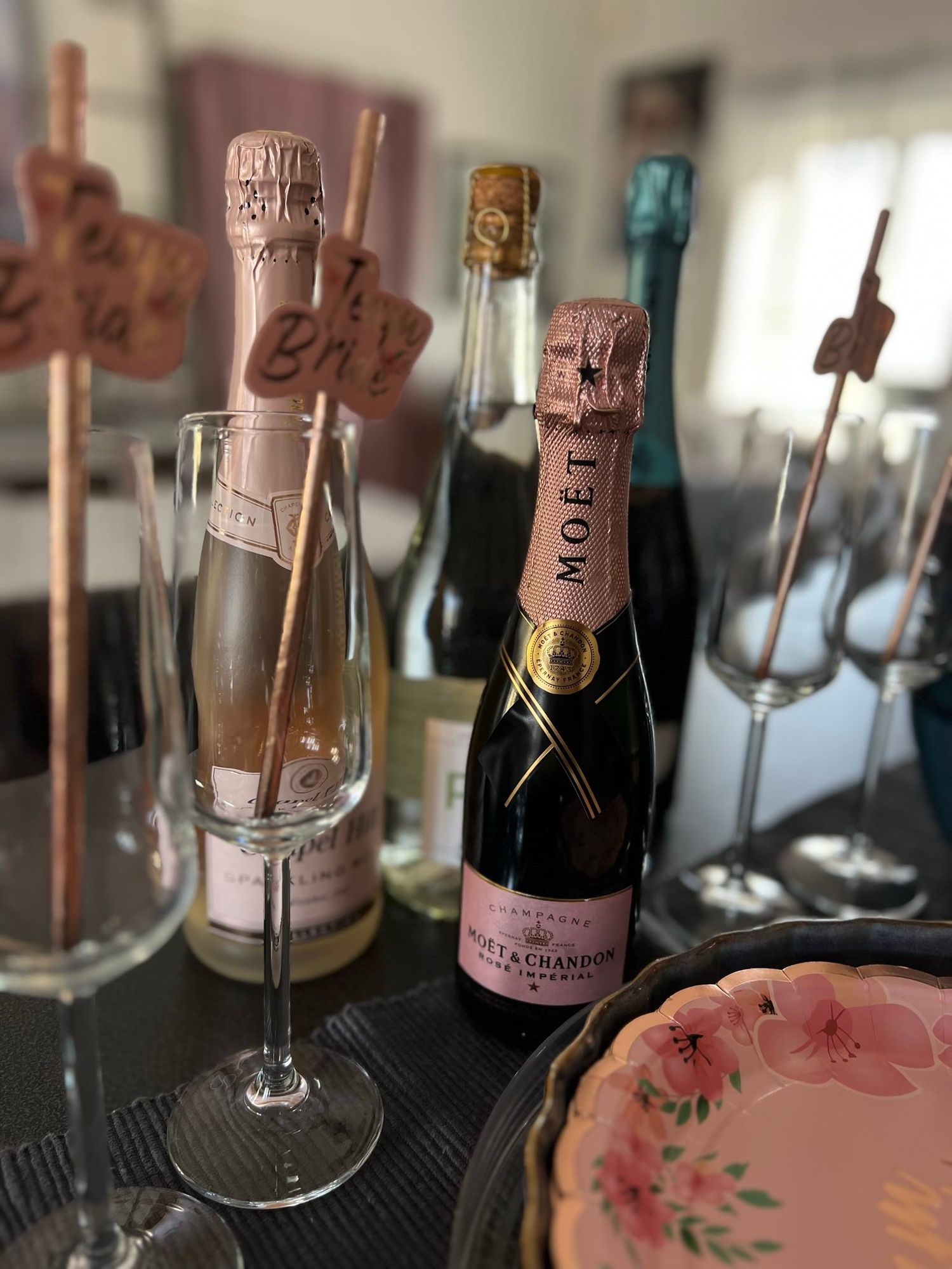 Champagne bottles and glasses arranged on a reflective surface with pink floral decor and soft lighting.