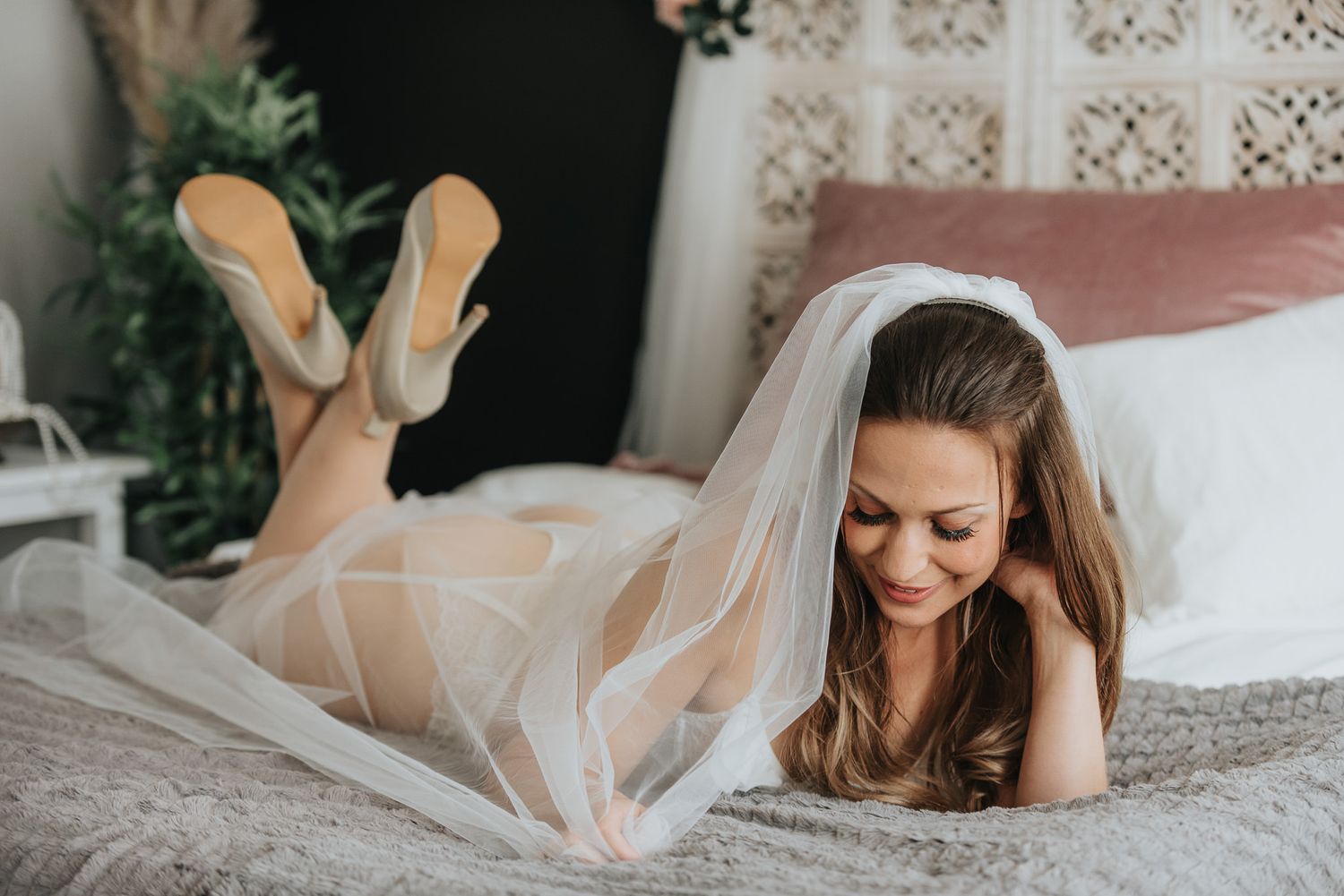 Brud med brudslöja i en sensuell pose i boudoirstudio.