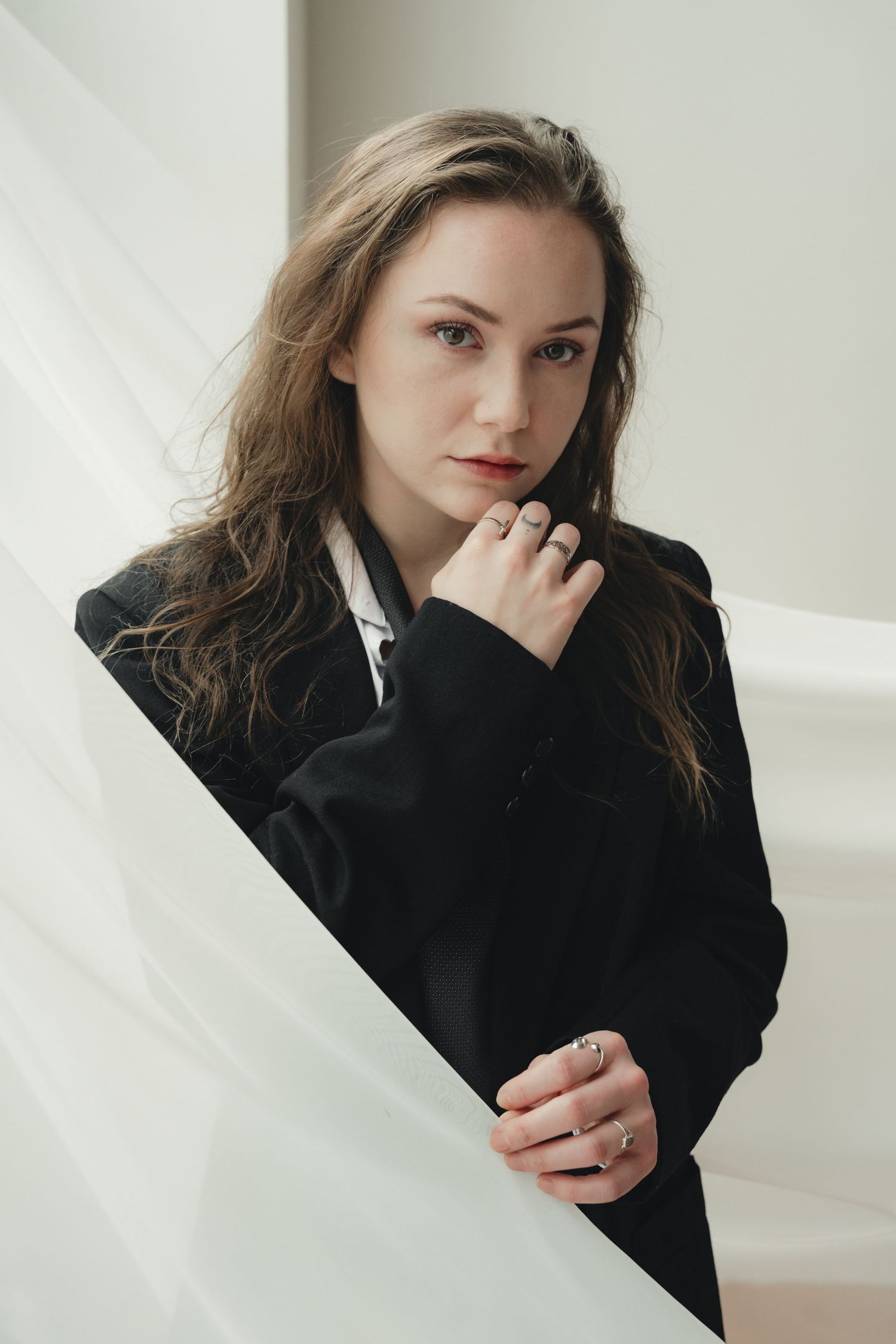 Minimalist portrait against white backdrop wearing black blazer in natural light.