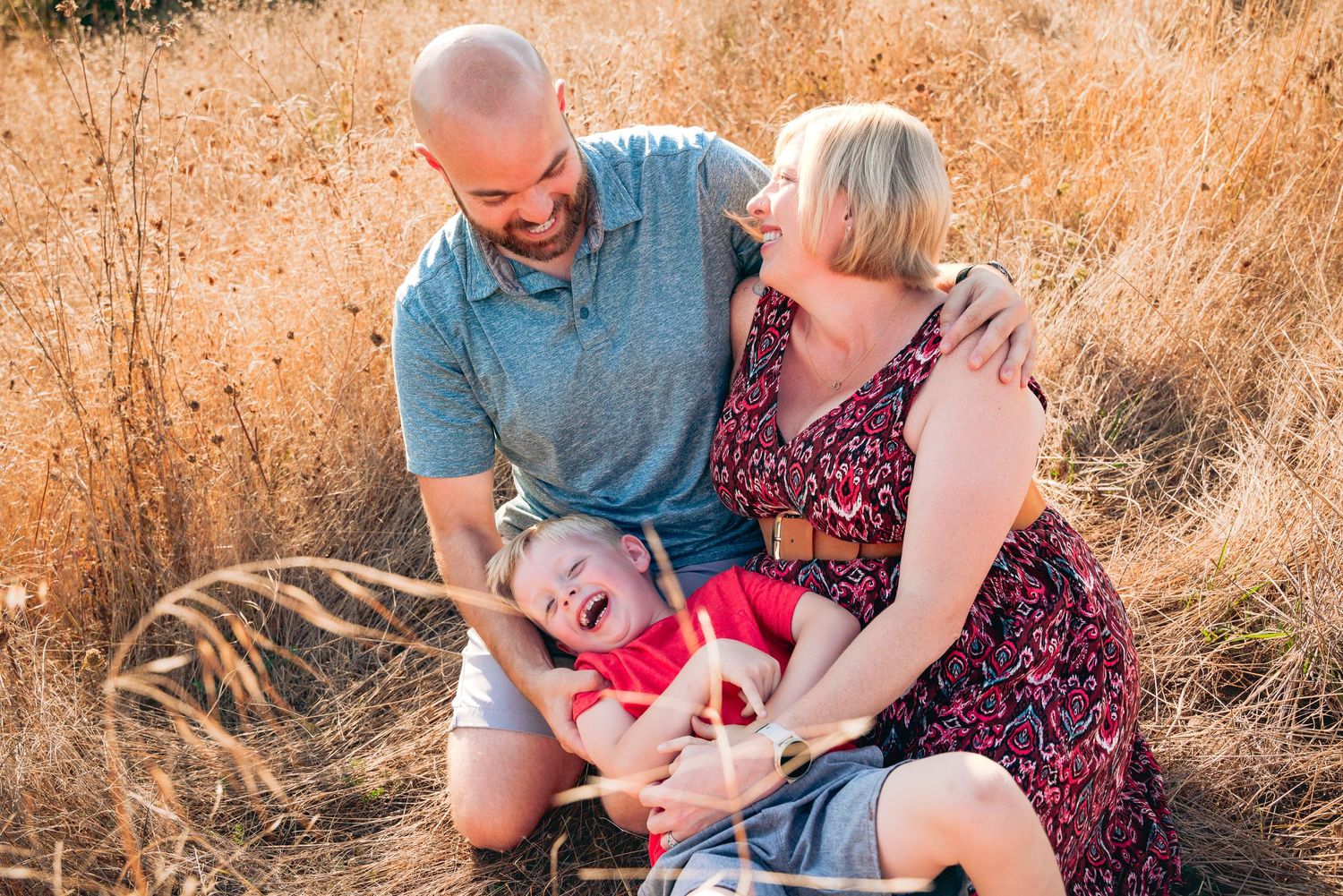 Family relaxing in golden grass field during sunset photoshoot.