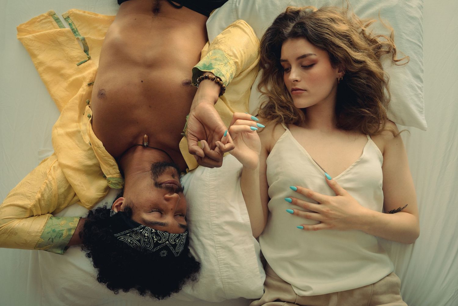 Artistic portrait of couple lying on white sheets in yellow and cream tones.