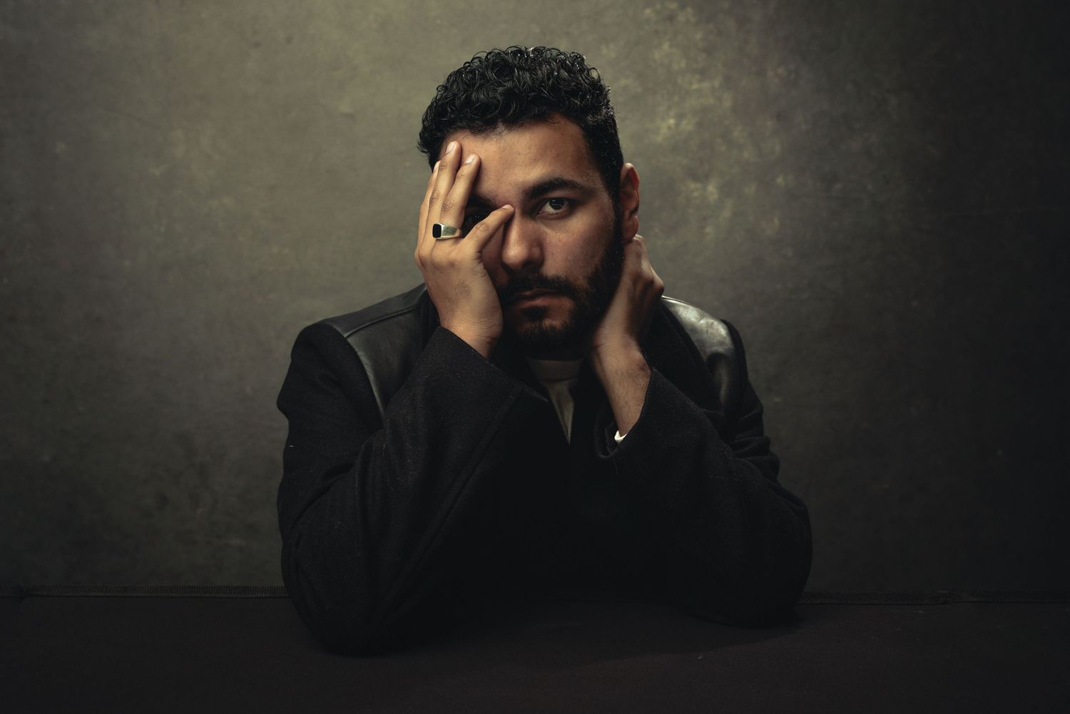 Dramatic low-key portrait showing emotional gesture against dark background.