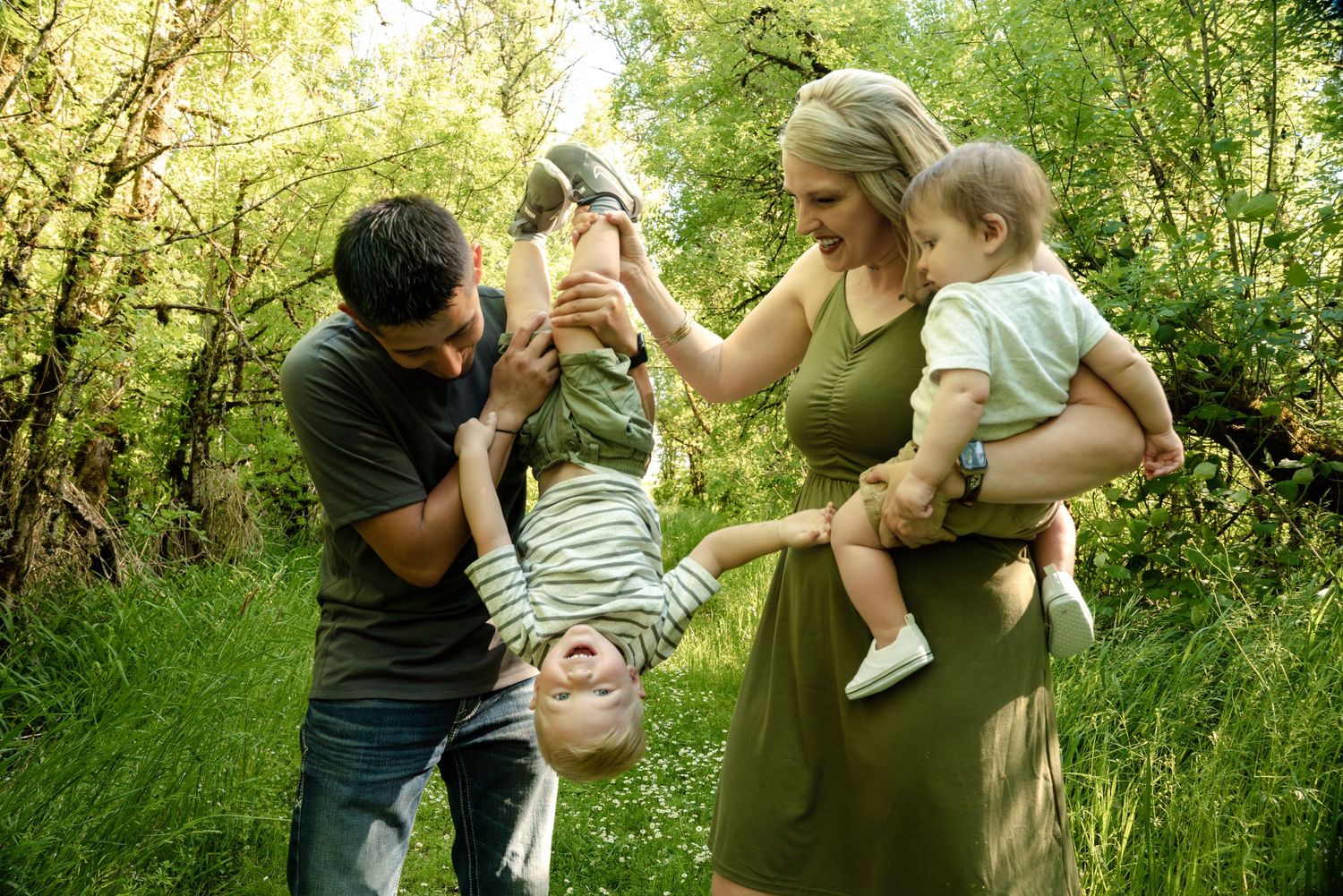 Playful family moment in lush green forest with parents holding children.