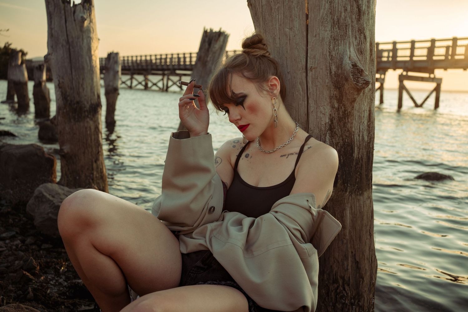 Moody sunset portrait by waterfront pier with casual lounging pose.