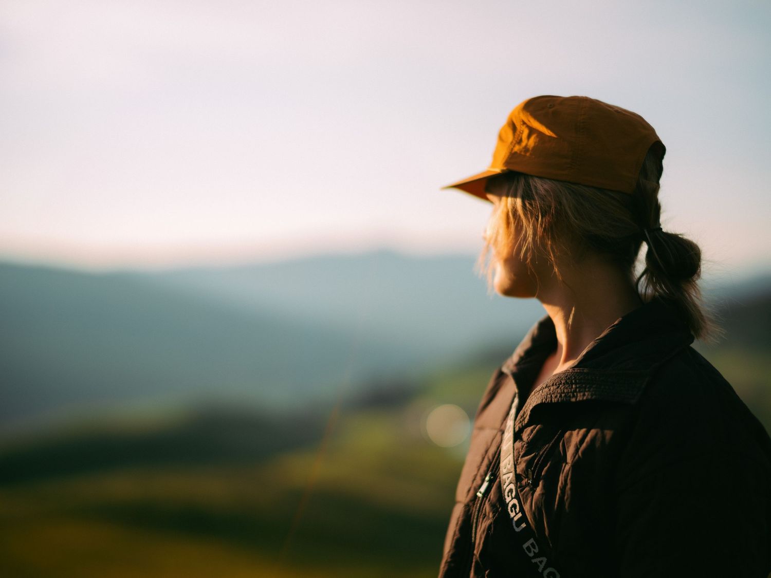 Person wearing orange baseball cap looking out over rolling hills at sunset.