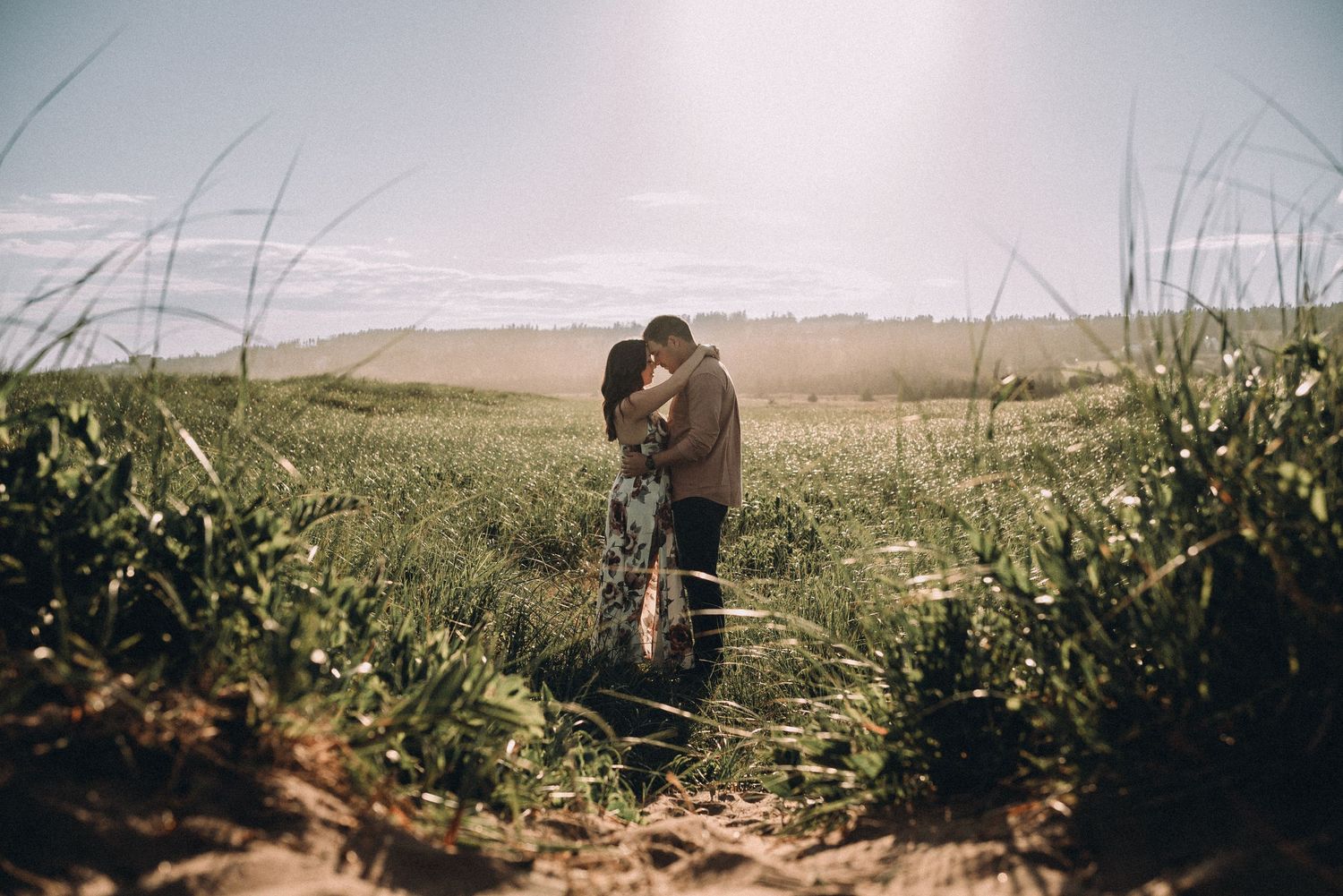 A couple embraces on a misty trail overlooking the ocean through tall grass and wild coastal vegetation.