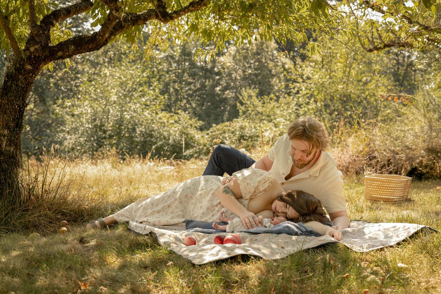 Couple enjoying a romantic outdoor picnic on a blanket under a tree in a sunny meadow with a basket nearby.
