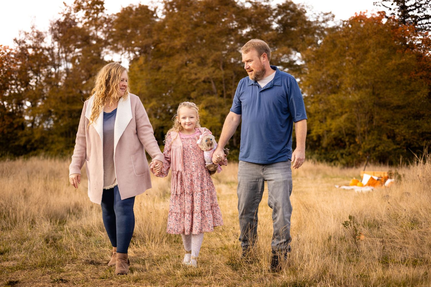 Family walking together through autumn field at sunset with golden light filtering through trees.
