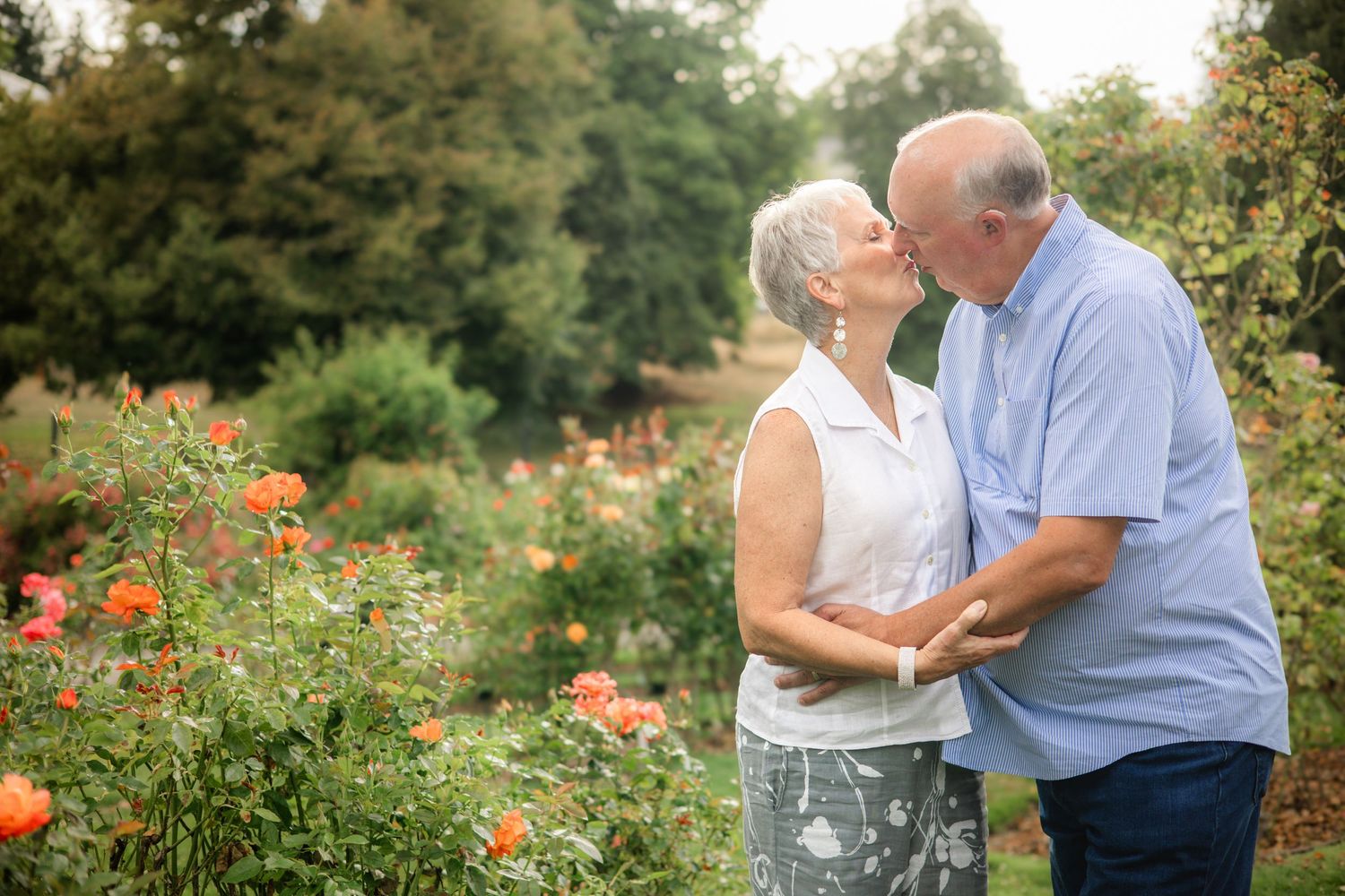 A couple embraces while standing in a vibrant garden filled with blooming red poppies and lush greenery.