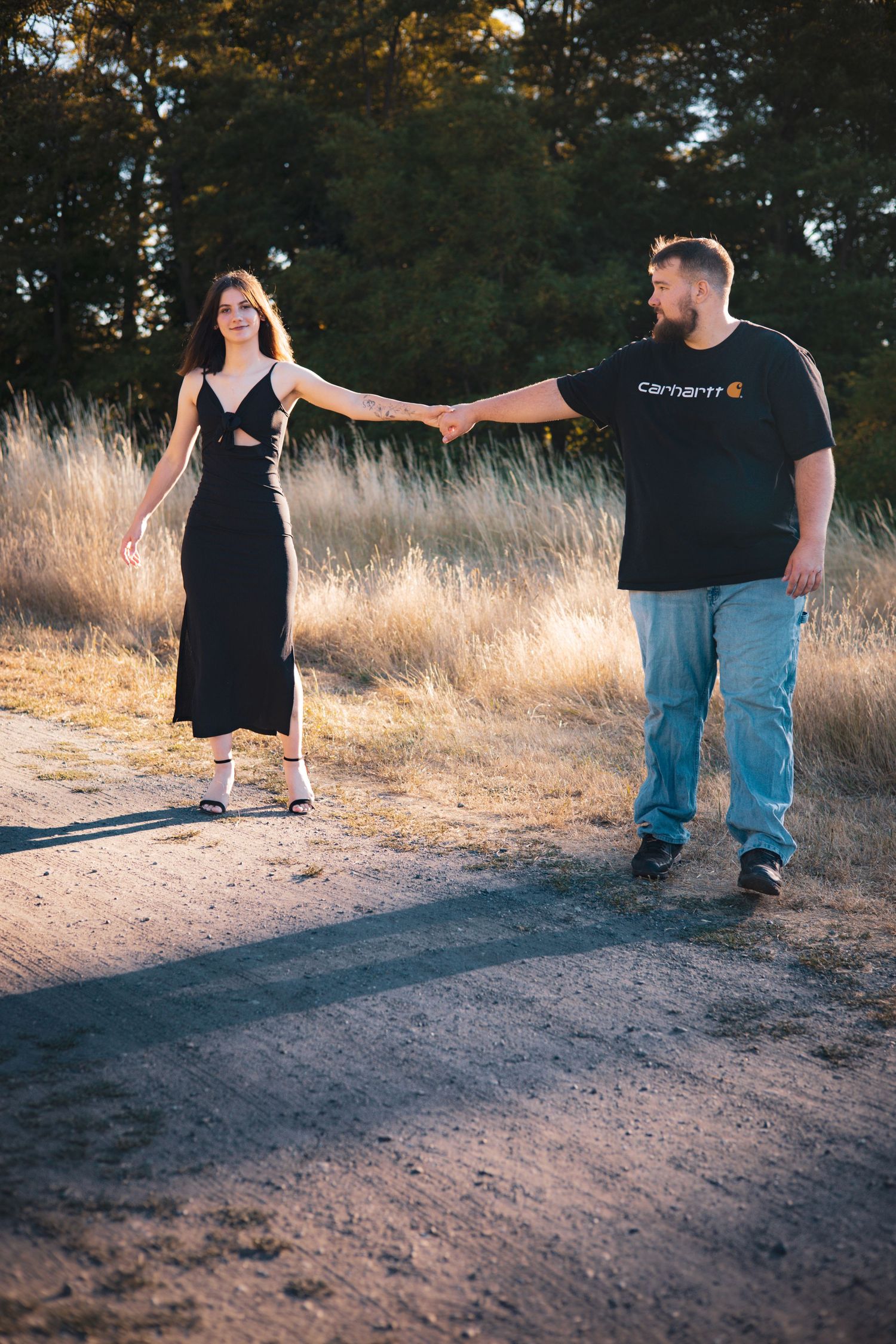 Couple walks hand in hand on dirt path during golden hour.