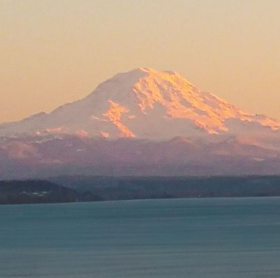 Snow-capped Mount Rainier glows pink at sunset over calm Puget Sound waters in Washington State.