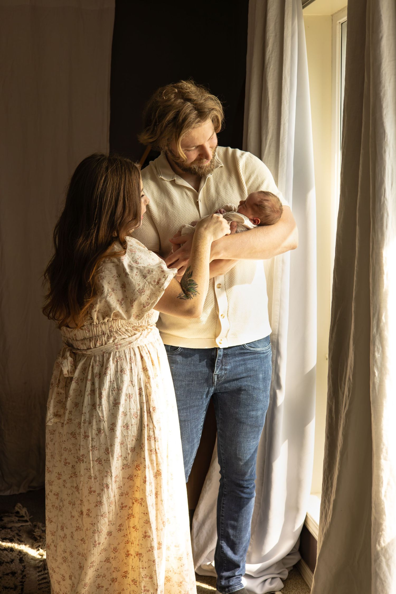 Mom and dad holding newborn together by window — lifestyle family photography in Tacoma, Gig Harbor, Puyallup, South Sound, WA