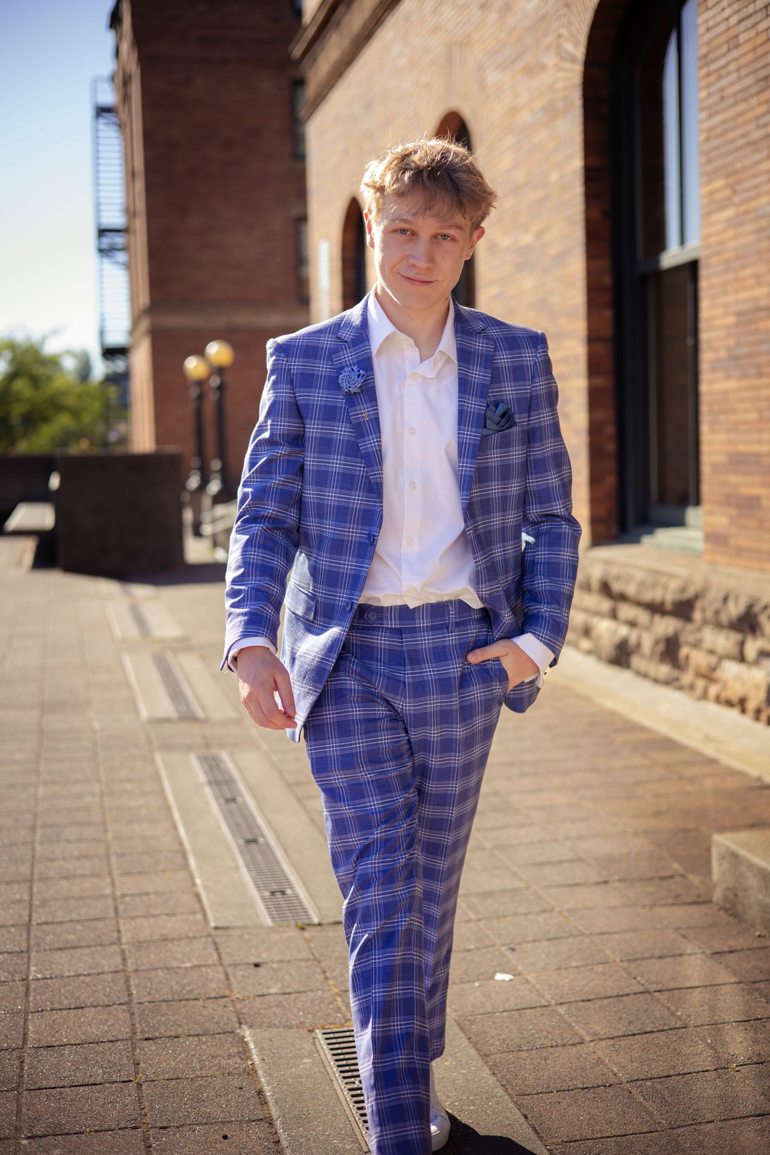 Person walking in a stylish blue checkered suit along brick building steps.