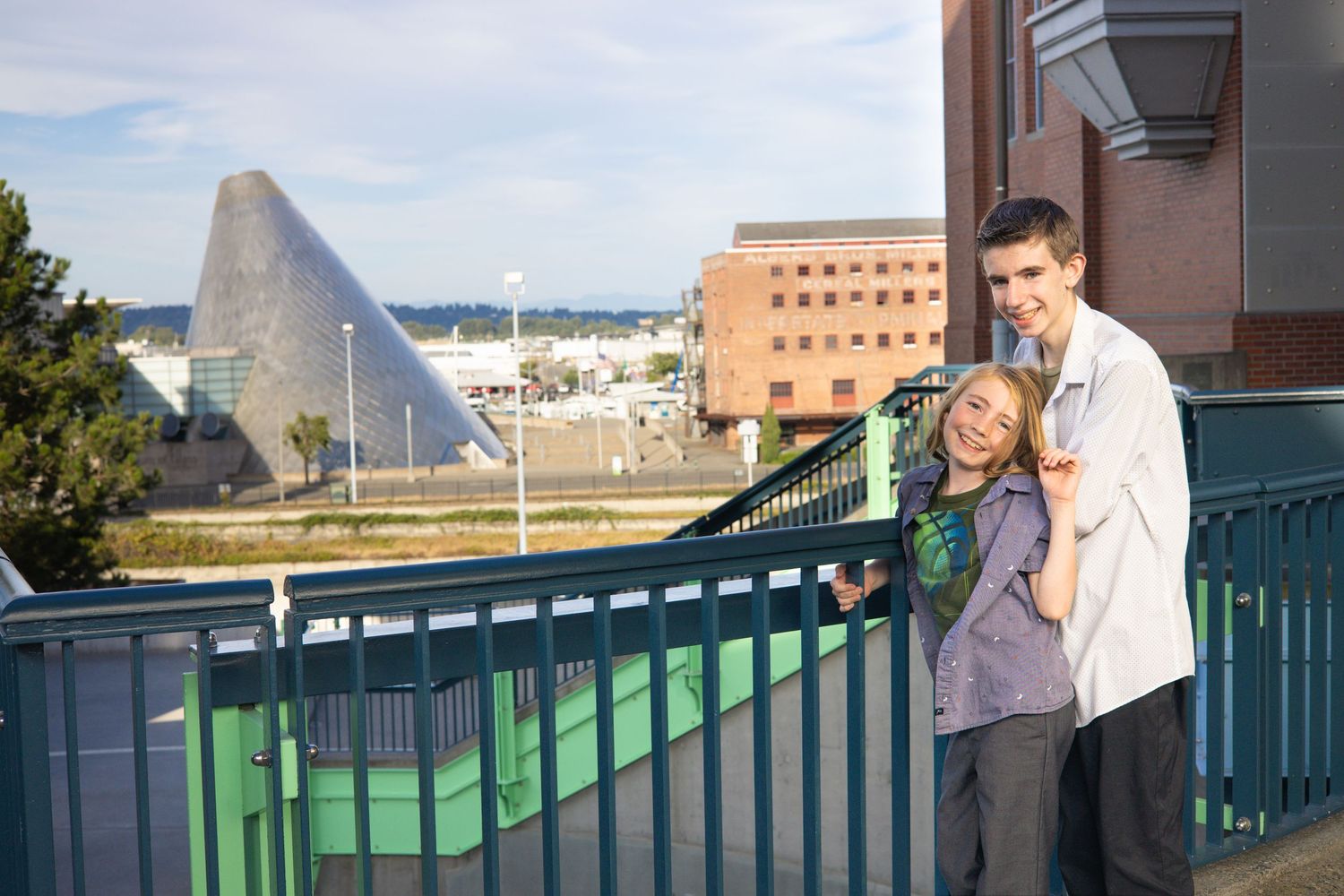 People standing by a green railing overlooking a cityscape on a bright day.