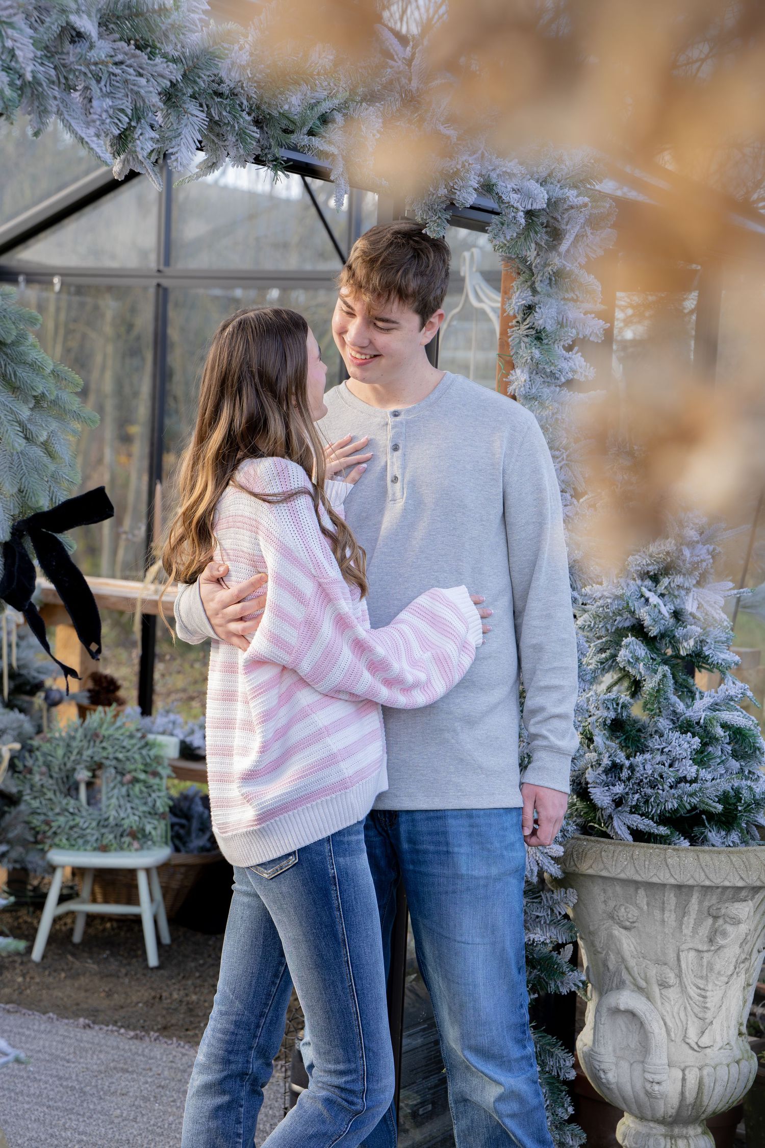 Romantic couple in casual winter outfits share tender moments in front of a greenhouse with frosted decor.