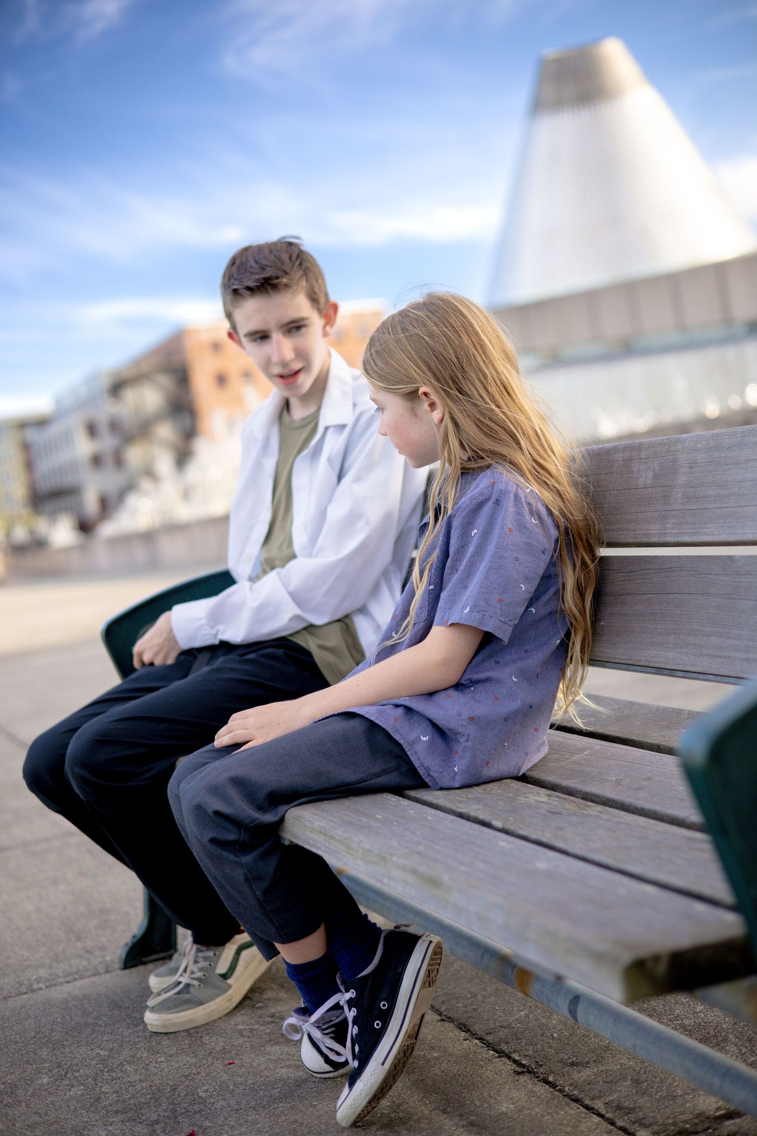 Two people sitting together on a wooden bench in an urban setting.
