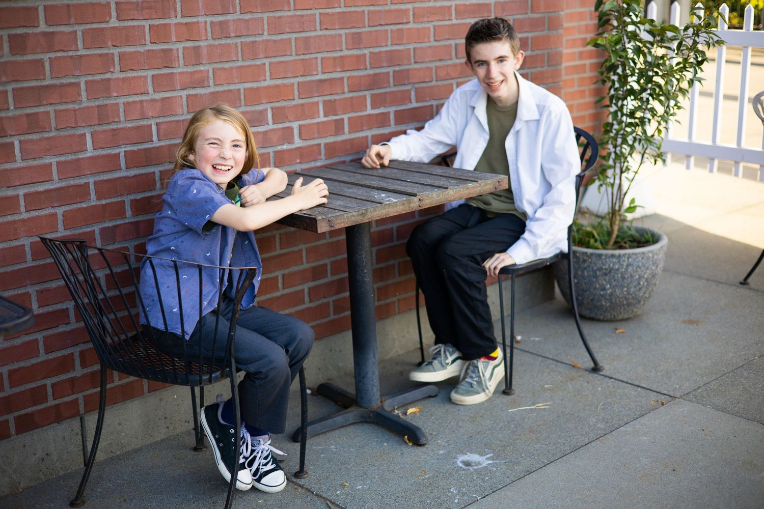 Two people sitting at a table outside a brick building on a sunny day.