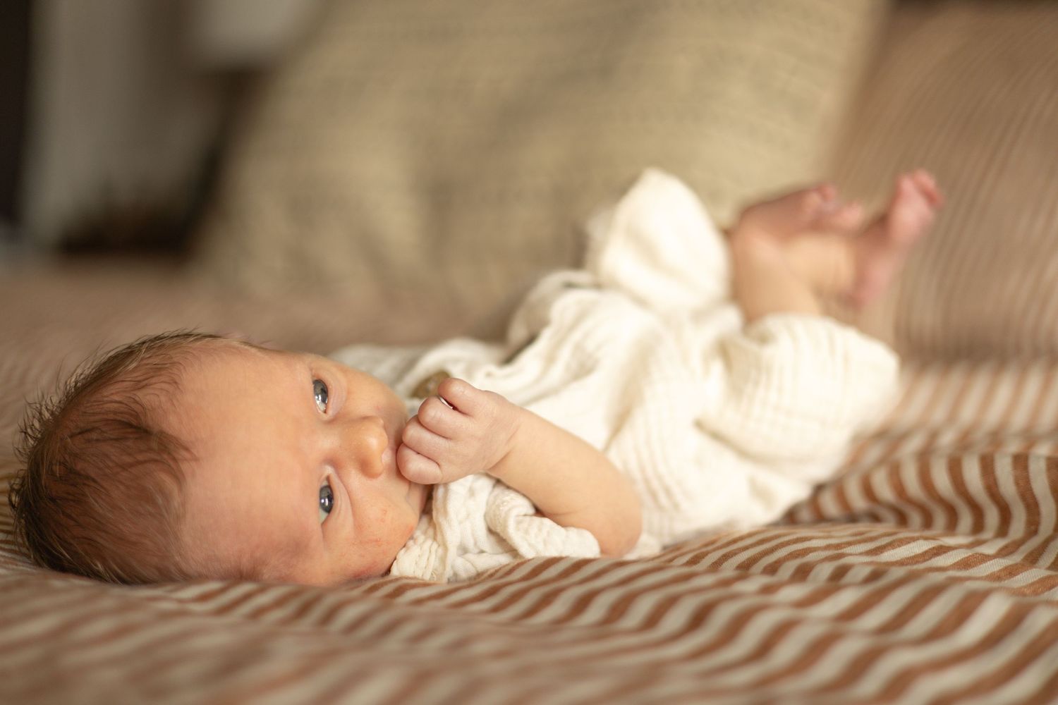 Newborn on bed with hand in mouth, looking to side — lifestyle photography in Tacoma, Gig Harbor, Puyallup, South Sound WA